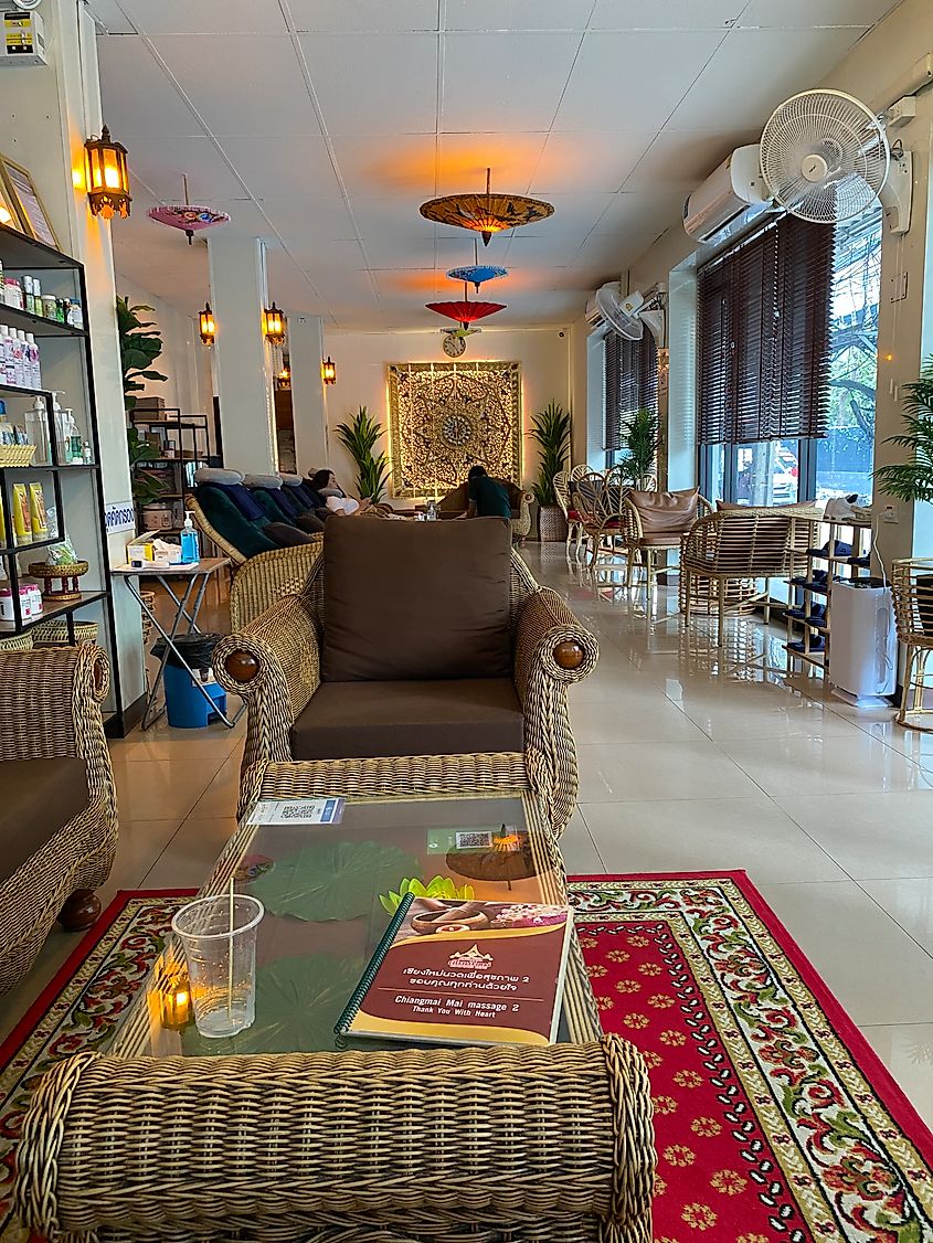 A first-person POV from inside a Bangkok massage parlor. A menu sits on the table and in the distance a woman is getting a foot massage.