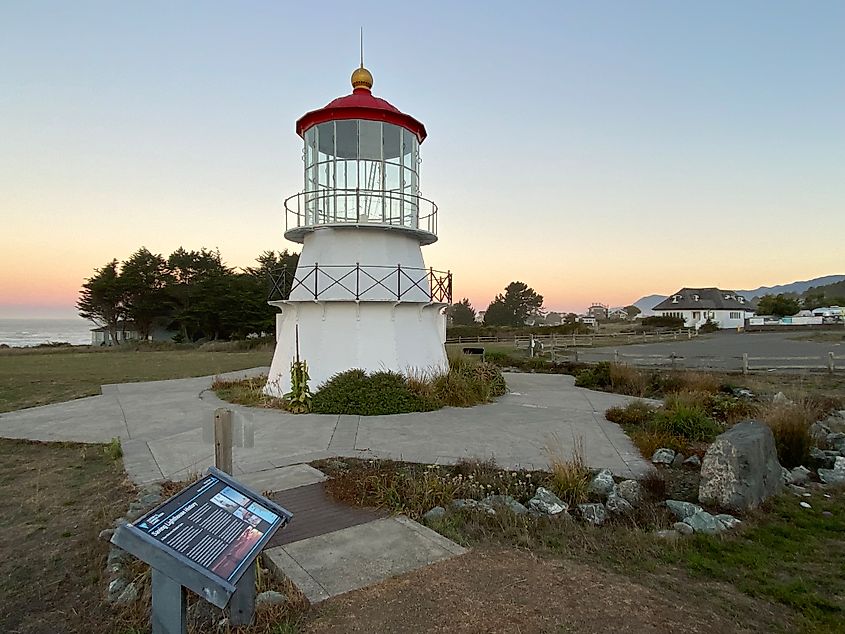 A stubby white lighthouse with red top stands against a pastel sky 