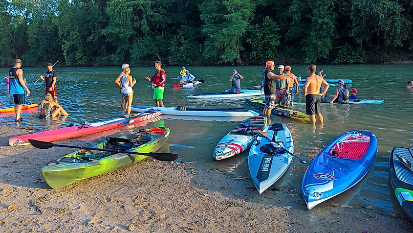 Participants near their paddle boards talk about their racing experiences after a stand-up paddle board event.