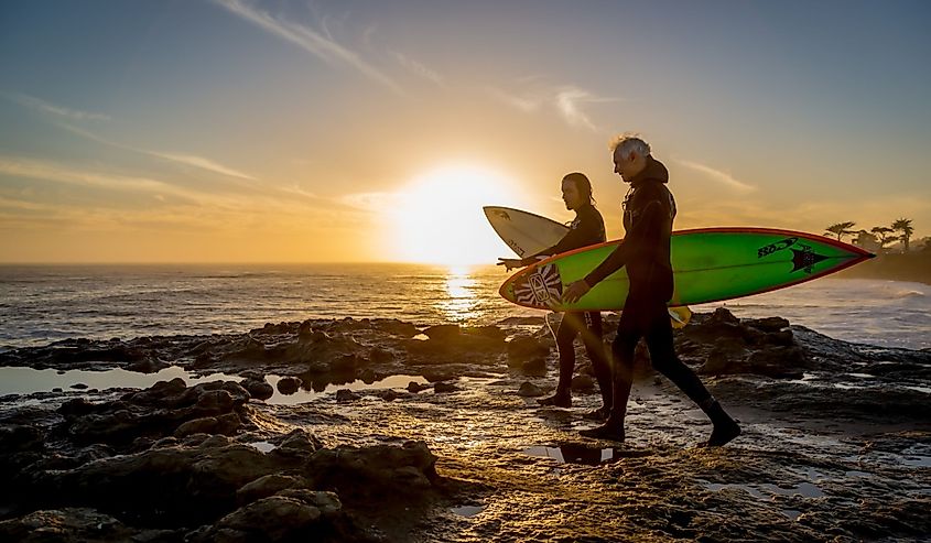  Two surfers walking with their surfboards with a nice sunset at the background in Santa Cruza, California