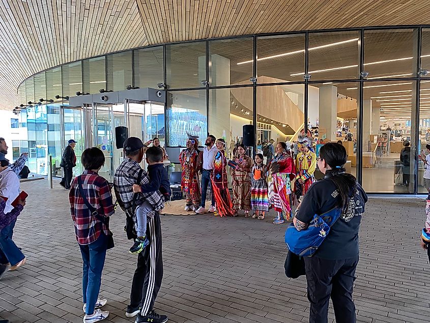 Indigenous people in traditional garb posing for pictures outside of the Calgary Central Library. 