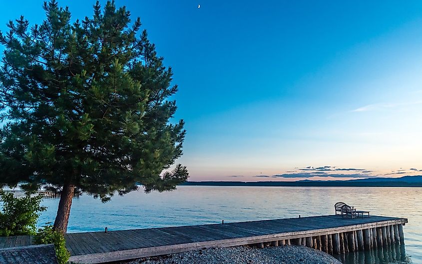 Sliver moon at dusk with a view of a wooden dock at the shoreline of Flathead Lake, near Polson, Montana