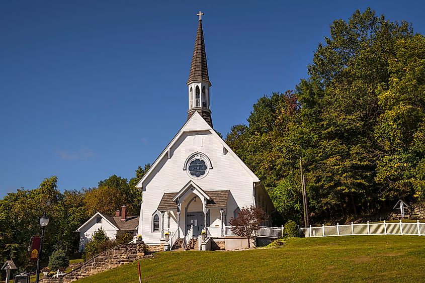 Front view of a quaint, rural church chapel in French Lick, Indiana, sitting atop a green hill. The idyllic small-town church features classic architectural elements, set against a peaceful countryside backdrop.