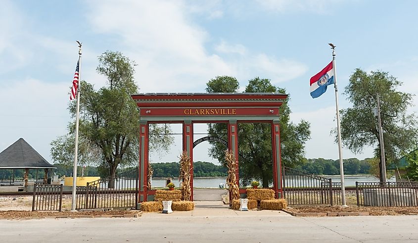 Red and green arch structure with town name Clarksville leading to edge of Mississippi River.