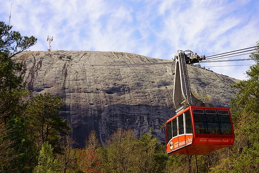 STONE MOUNTAIN, GEORGIA, USA - MARCH 19, 2019: Red Skyride cable car in front of Stone Mountain Summit with famous rock relief, the largest bas-relief in the world. The carving is a major attraction.