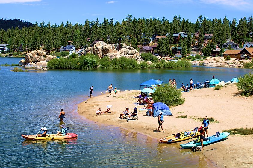 People kayaking beside a sandy beach cove in Big Bear Lake, California, enjoying recreational activities at the lake.