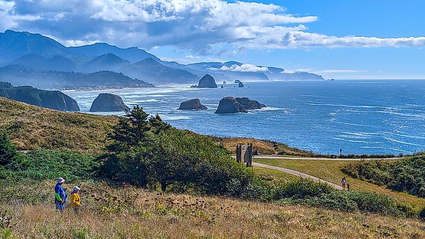 A vibrant coastal landscape featuring rolling hills and rugged cliffs along a blue ocean, with some people walking and enjoying the sunny day.