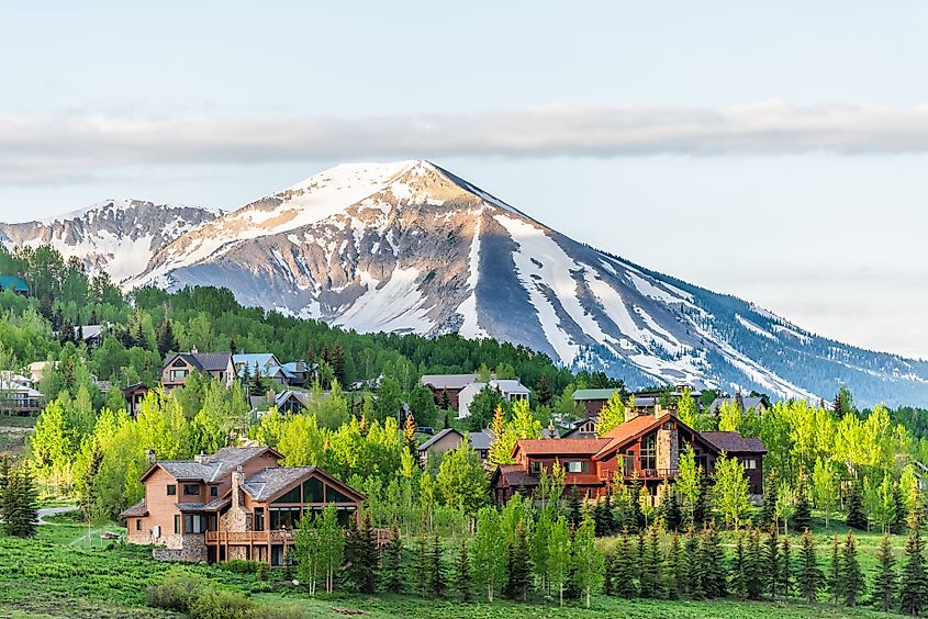 Mount Crested Butte, Colorado: A summer sunrise over a village with colorful wooden lodging houses nestled on hills surrounded by green trees.