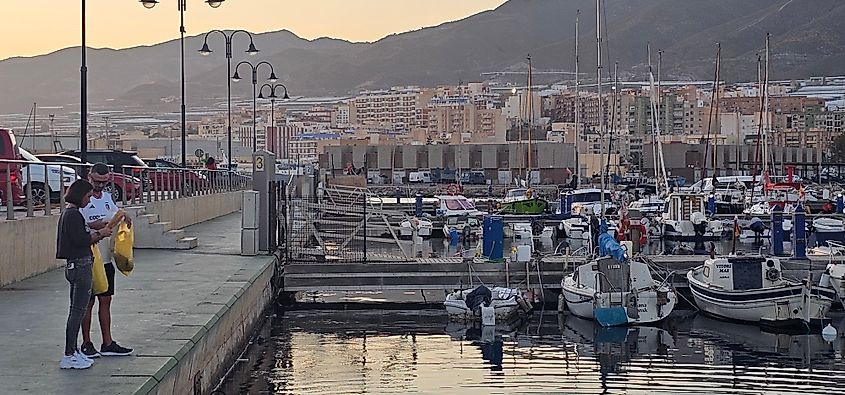 Evening view of Adra marina in Andalusia, Spain, with boats moored at the pier and people standing along the quay