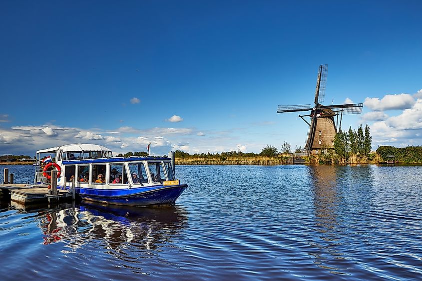 A tourist boat on the water canal in Kinderdijk with a windmill