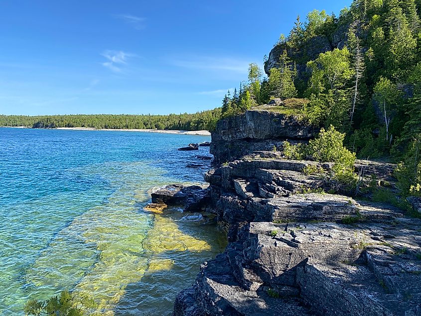 Limestone cliffs meet the turquoise waters of Georgian Bay on a clear sunny day.