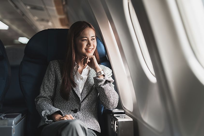 A young Asian woman sitting in a plane and looking outside.