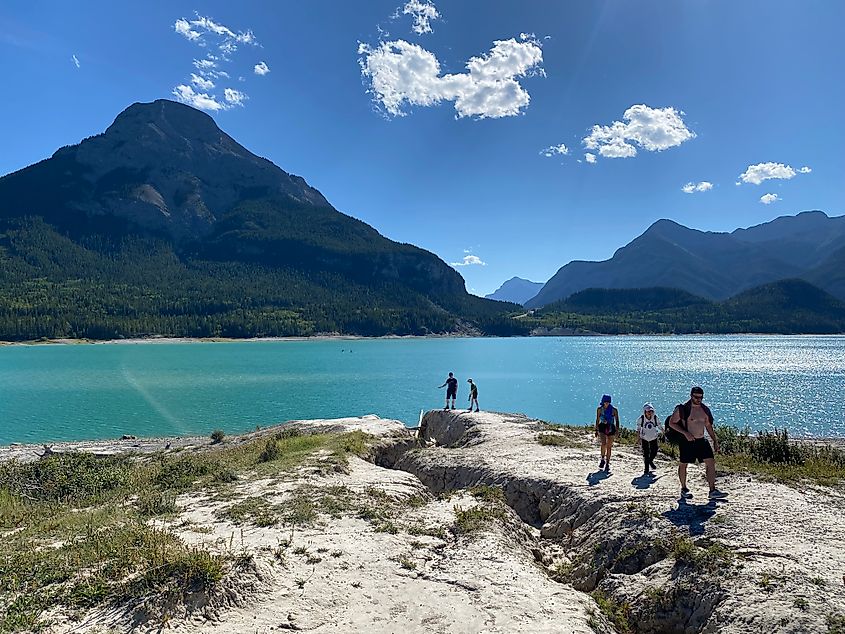 A handful of hikers walking up from a shimmering alpine lake bathed in sun. 