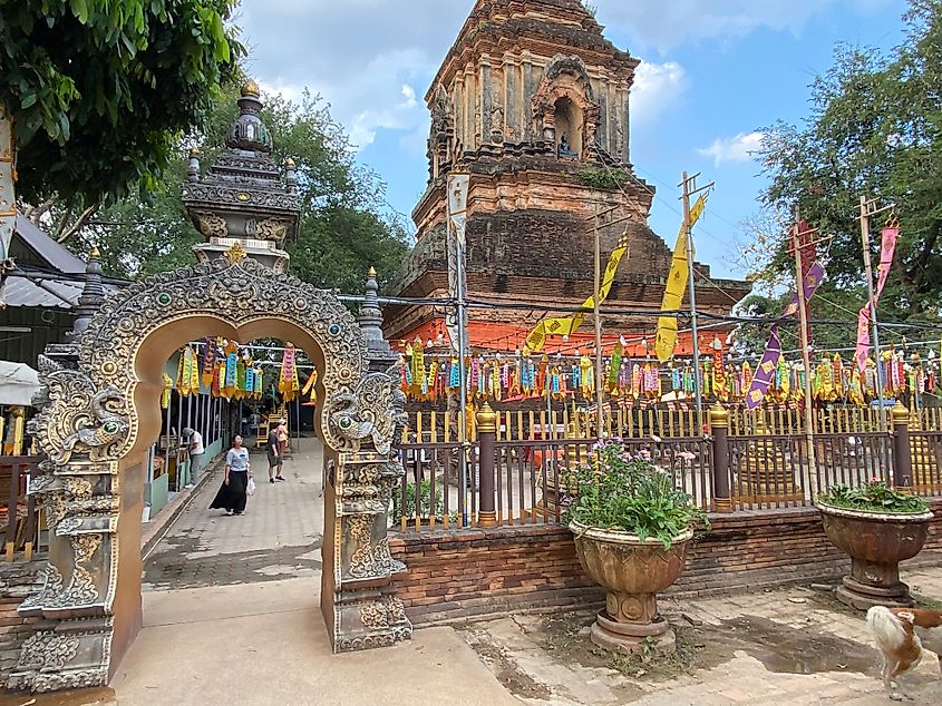 An Asian woman walks toward the gate of an ancient stone stupa. The courtyard is decorated with brightly colored flags.