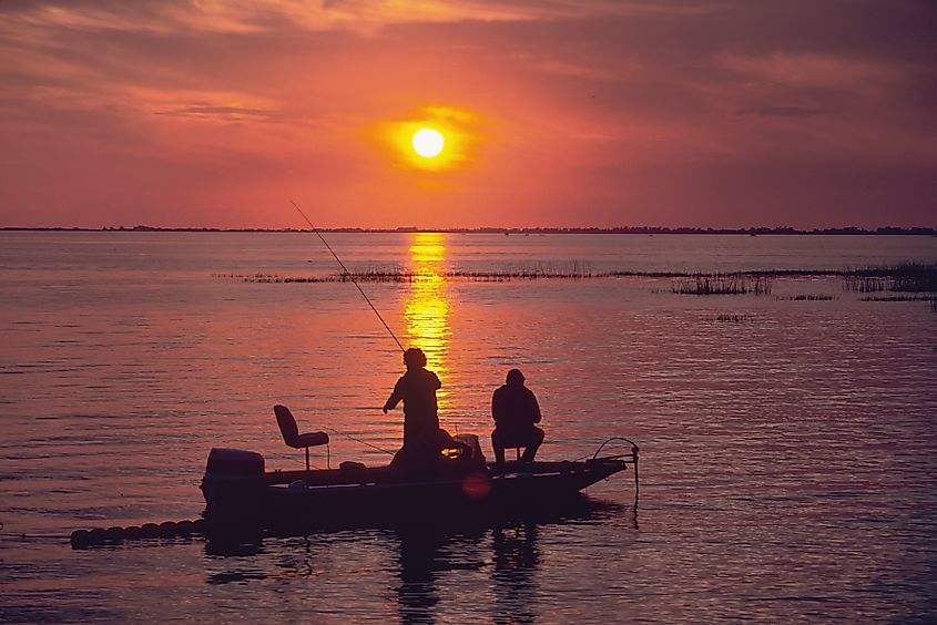 Family fishes for bass from a boat at sunset on Lake Okeechobee, Florida. Editorial credit: Dennis MacDonald / Shutterstock.com