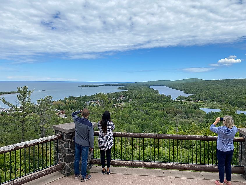 A few tourists taking in the forest and waterfront views from atop a mountain platform.