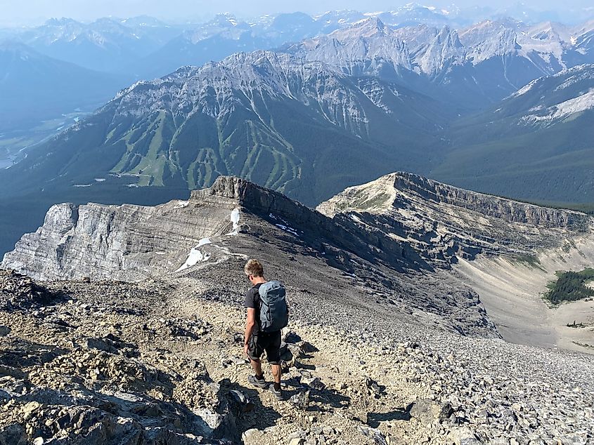 A male backpacker walks down the rocky slopes of a large mountain in Banff National Park. 