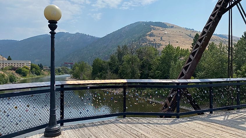 A pedestrian bridge overlooking a wide river and mountain with a white, capital M, showing near its summit. 