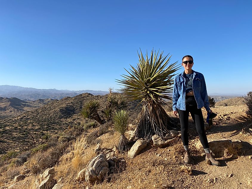 A young woman stands atop a desert mountain peak