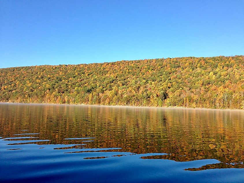 The clear, still water of Canadice Lake, one of the Finger Lakes in New York, in autumn, with a blue sky in the background.