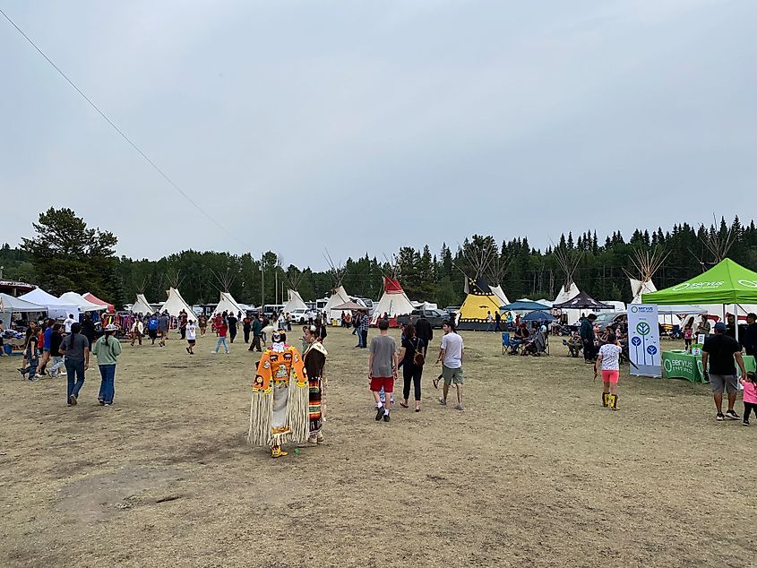 Indigenous people and powwow casual attendees stroll tipi-lined festival grounds.  