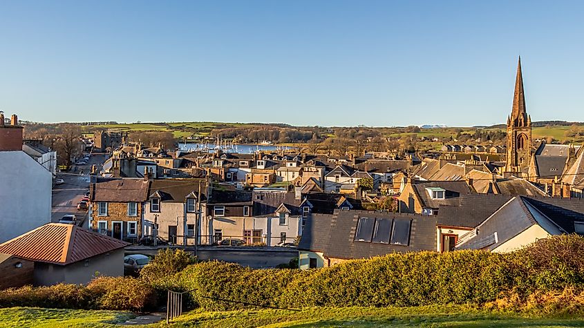 A view over the artist and fishing town of Kirkcudbright in Dumfries and Galloway, Scotland, featuring colorful buildings, a quaint harbor, and the surrounding lush countryside.