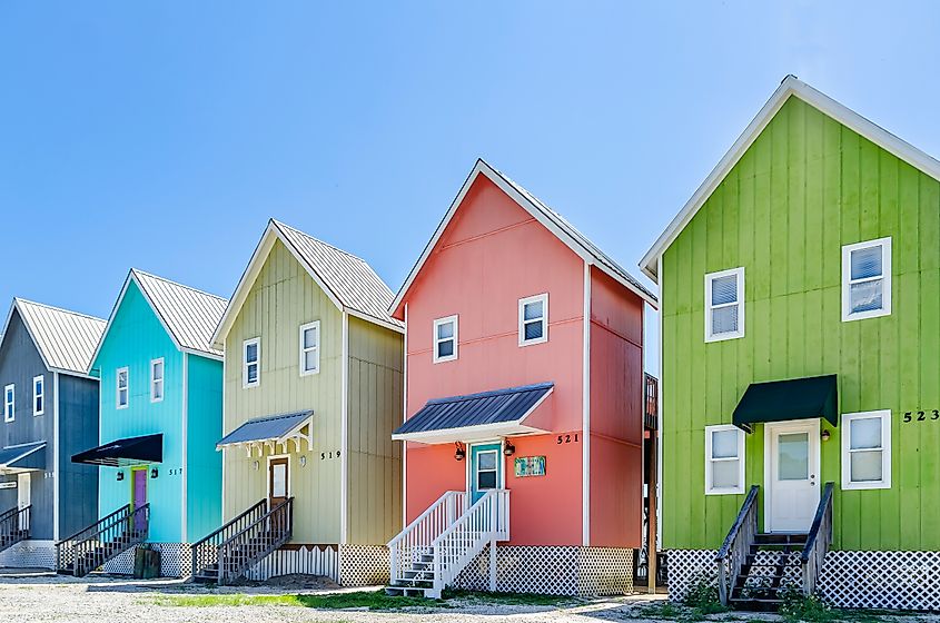 A row of colorful beach houses, known as “The Birdhouses,” overlooking Bayou Aloe in Dauphin Island, Alabama. Originally built as fishing camps, these homes add vibrant charm to the coastal landscape.