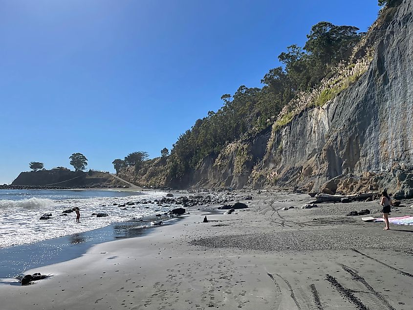 A sheer cliff frames a beautiful oceanside beach on a sunny day. 