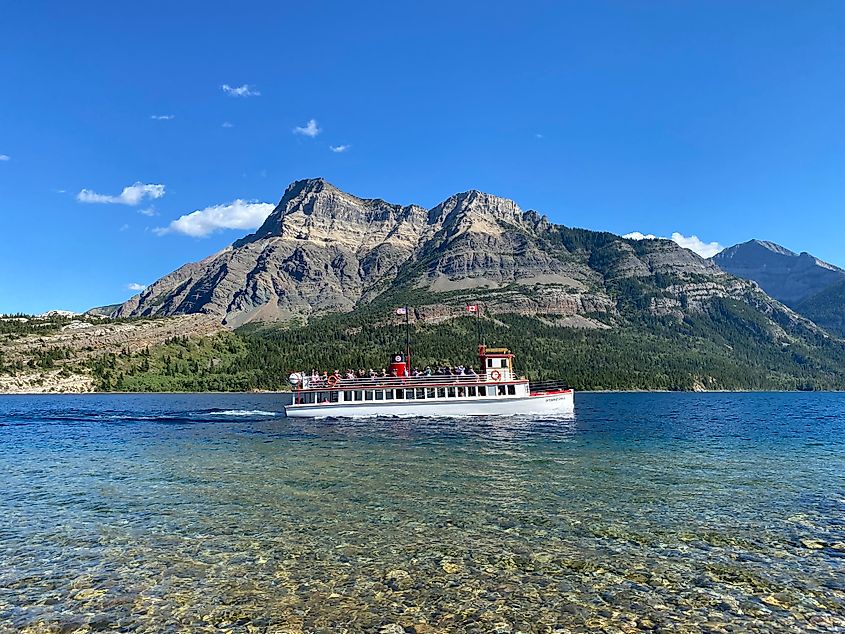 An old fashioned lake tour boat passes by a large mountain