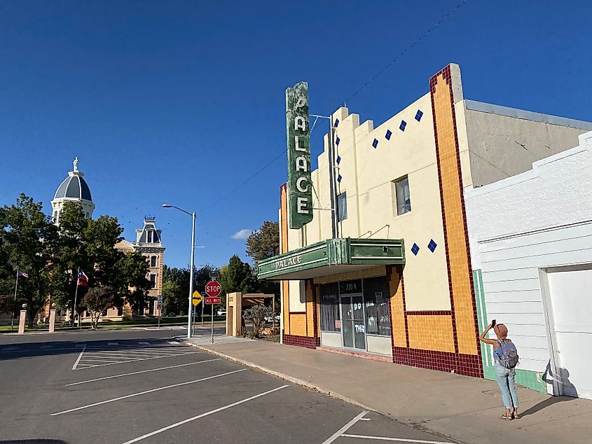 A woman in an orange beanie takes a picture of a run-down movie theatre called the Palace. 