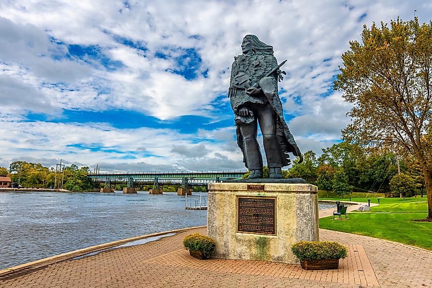A large riverside statue of an indigenous (Potawatomi) chief watching over a wide, flowing river.