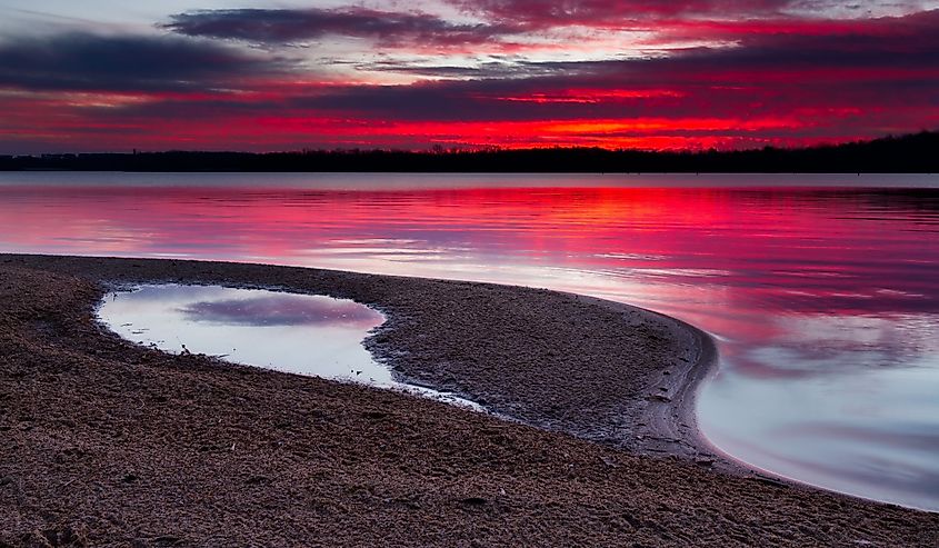 A horizontal image of sunrise on a sandy shoreline of Longview Lake near Sunrise Beach.