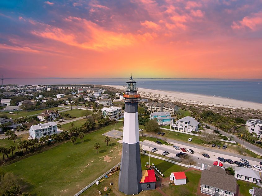 Aerial shot of the gorgeous spring landscape at Tybee Island Beach, featuring the lighthouse, blue ocean water, sandy beach, homes, and lush green trees and grass in Tybee Island, Georgia, USA.