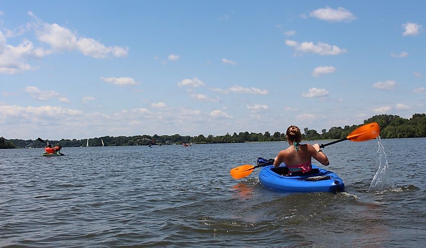 Girl in kayak paddling on Lake MacBride Iowa on a sunny day with small puffy clouds in clear blue sky on calm waters near Solon, Iowa.