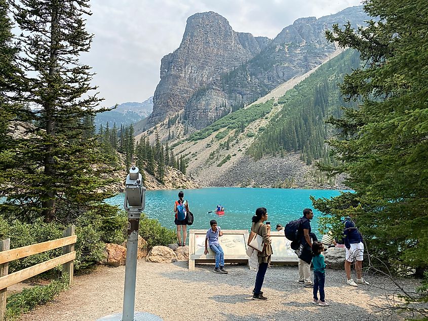 A mounted viewing station and a small crowd of people stand before a pristine mountain lake.