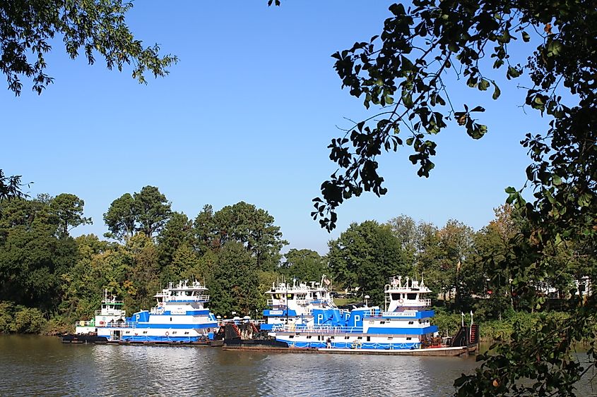 Black Warrior River in Alabama with ships navigating the calm waters, surrounded by lush greenery and a distant tree-lined shoreline.