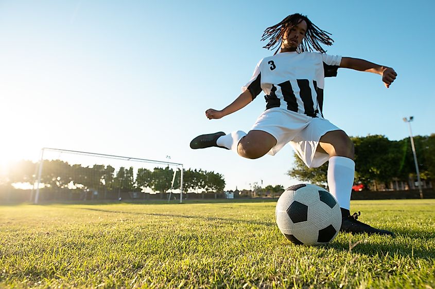 Young adult soccer player kicking soccer ball on soccer field