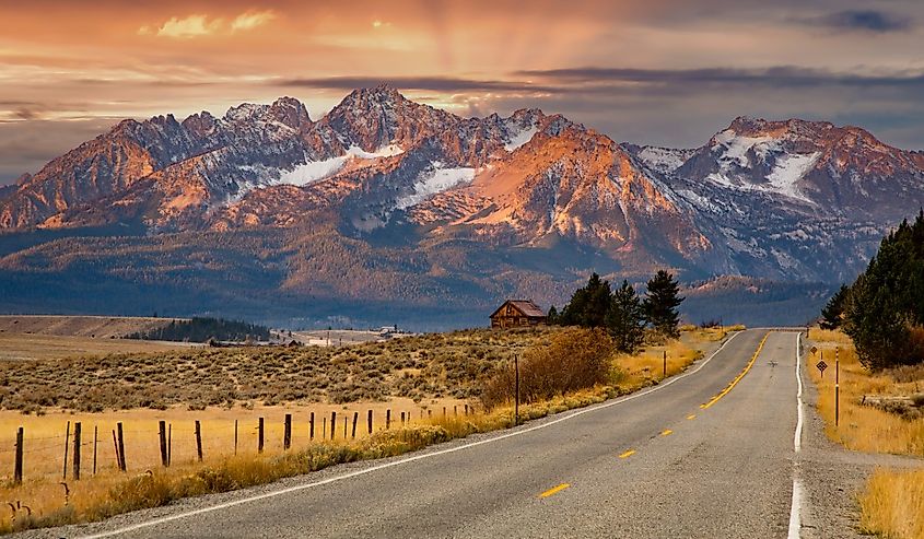 The Sawtooth mountains and a log cabin at sunrise and highway 75 leading to Stanley, Idaho.