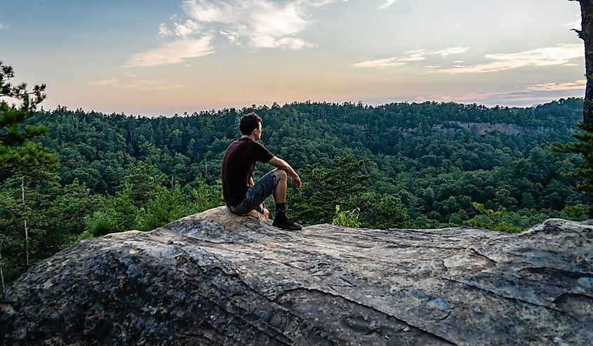 A young man sits on an outcropping of rock atop a mountain in Red River Gorge, Daniel Boone National Forest, Kentucky.