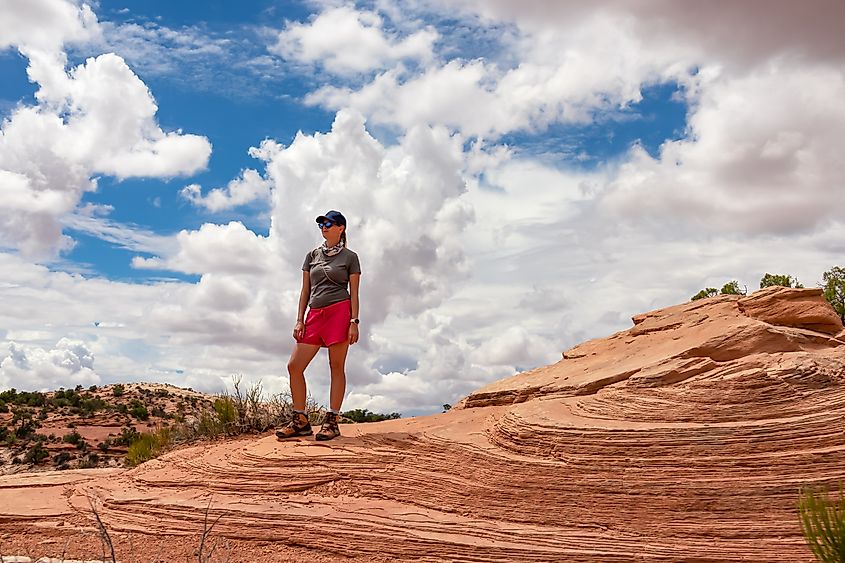 Woman standing on layered rock formation near Mesa Arch, Moab, Canyonlands National Park, Utah, USA. 