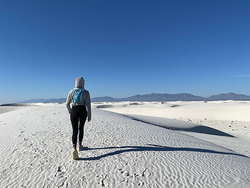A hooded hiker walks through the gypsum dune field of White Sands National Park