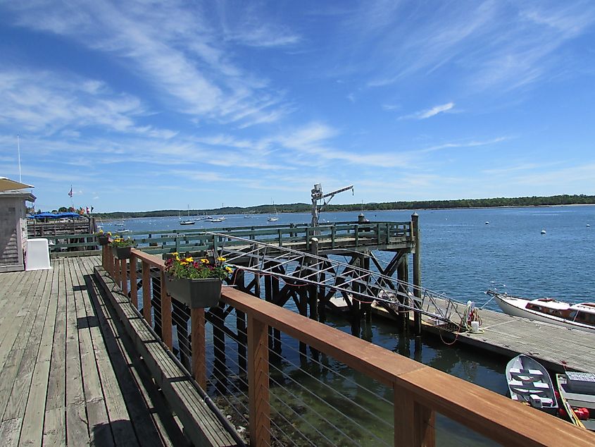 View of the Castine, Maine waterfront from picnic tables, overlooking the harbor with boats docked and scenic water views framed by trees and the shoreline.