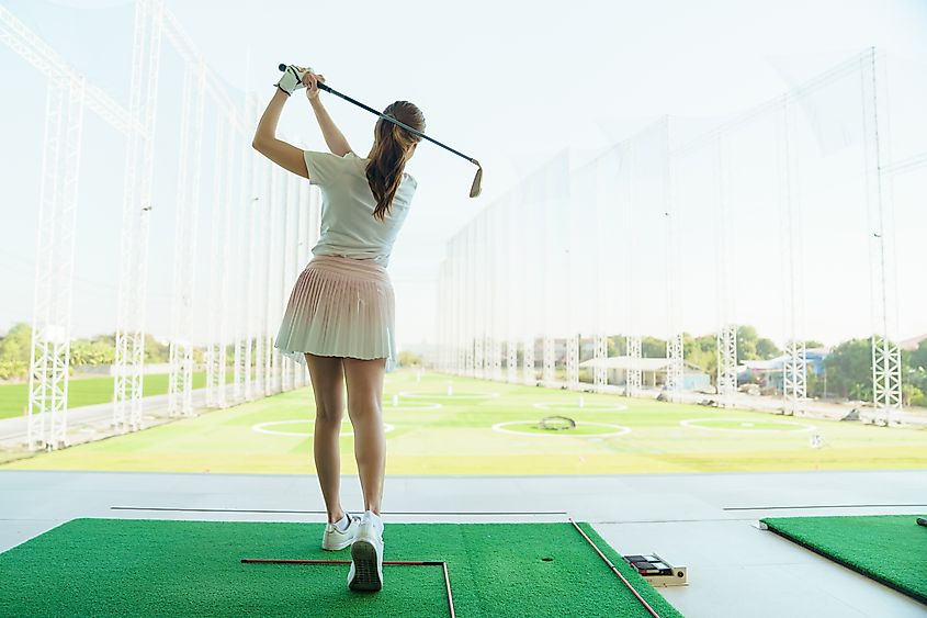Rear view of female golfer finishing swing at driving range.