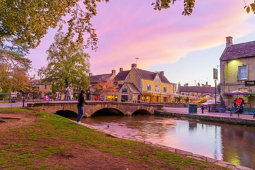 Sunset scene of typical houses, the river Windrush, locals and visitors, in the village Bourton-on-the-Water, the Cotswolds region, England