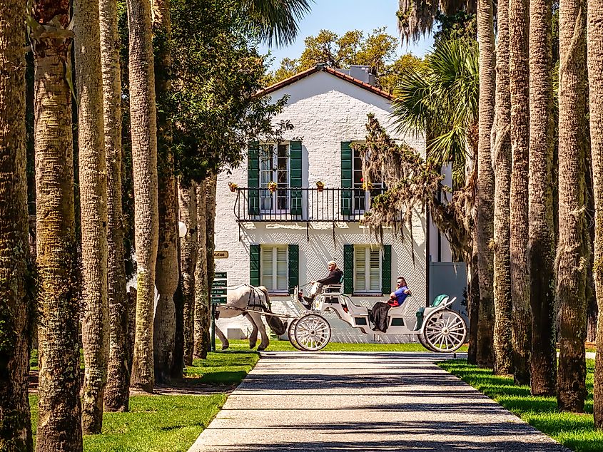 A guide takes a couple on a leisurely horse-drawn carriage tour past Crane Cottage in Jekyll Island, Georgia.