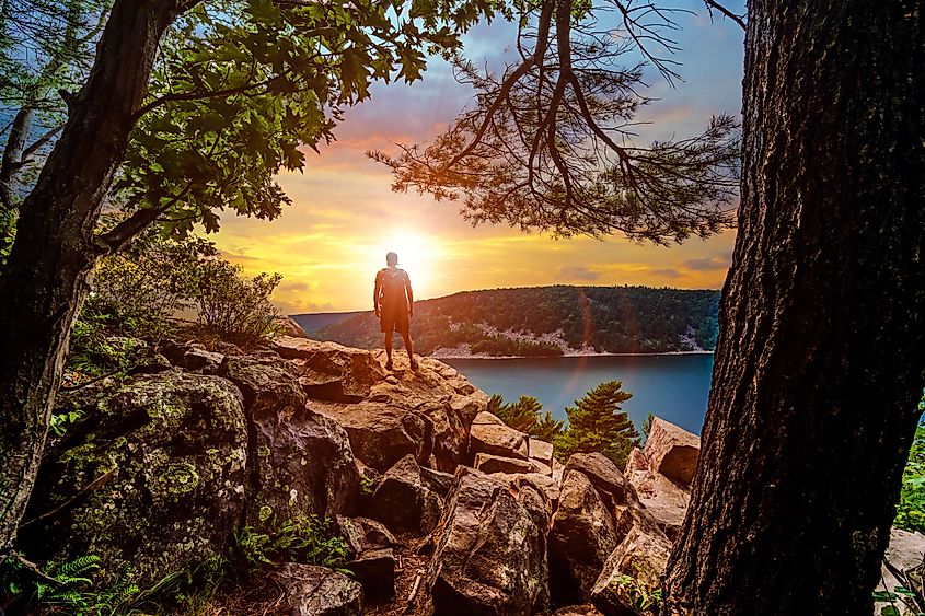 A silhouette of a man looking out into the sunset over Devils Lake State Park from a hiking viewpoint in Baraboo, Wisconsin, USA.