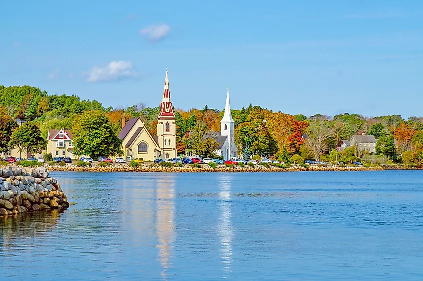 Peaceful waterfront with two churches framed by autumn trees in Mahone Bay, Nova Scotia.