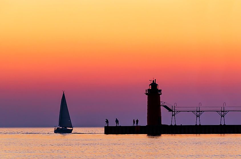 A colorful twilight sky silhouettes a sailboat, people, and the lighthouse at South Haven, Michigan, on Lake Michigan