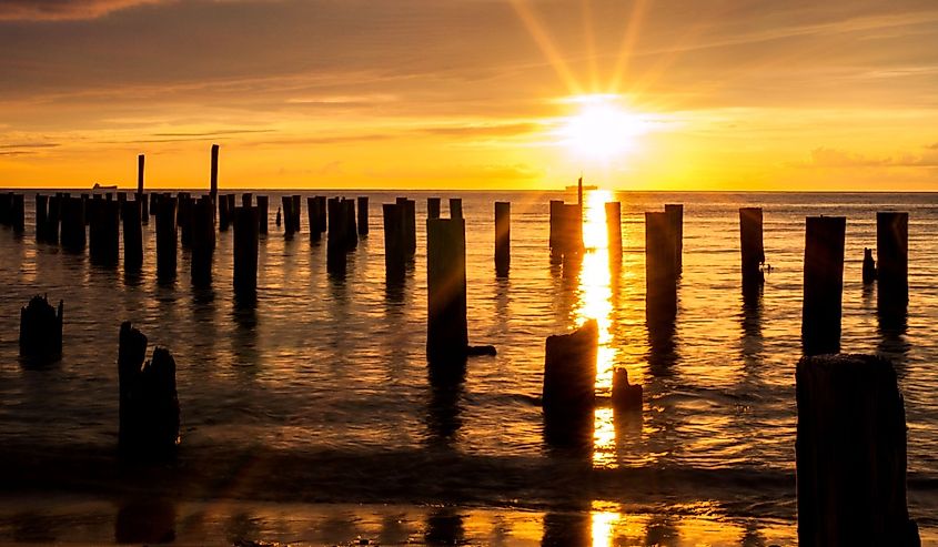 A ship crosses under the sun making a cross with the posts from an old ferry dock during sunset at Cape Charles Virginia in the Chesapeake Bay.