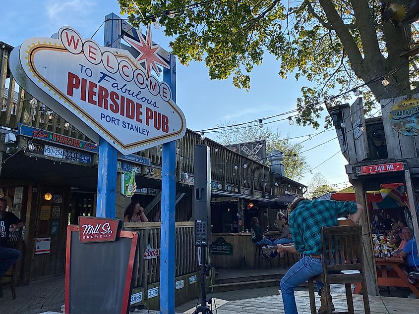 A solo acoustic musician plays on a wooden stage to a small crowd at a beach bar called Pierside Pub